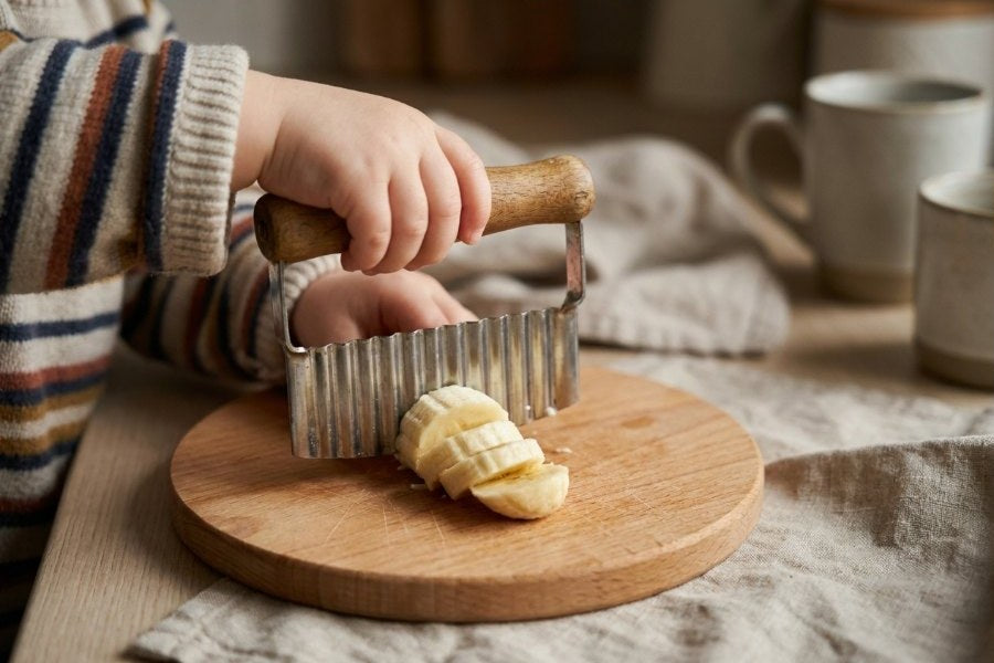 Kind schneidet Banane mit dem Wellenschnittmesser, beide Hände am Griff